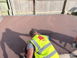 In-progress shot of an AAS Group Construction technician hand-troweling a new reddish-brown resin bound surface in Wellingborough, Northamptonshire