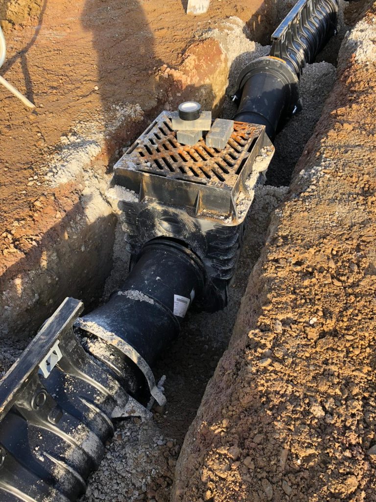 Heavy-duty commercial drainage gully pot with iron grate installed in aggregate trench for car park drainage at Rushden Lakes