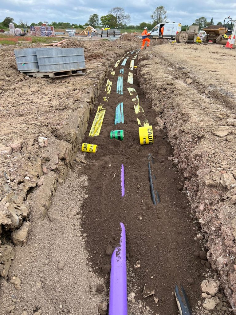 Close-up view of an excavated utility trench featuring yellow gas and electric caution tapes alongside green telecommunications warning tape