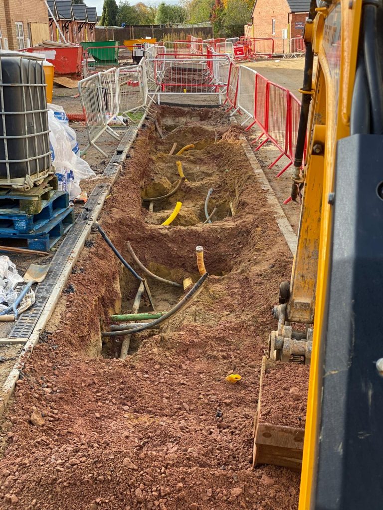 Exposed underground utility pipes and conduits including gas, electric, and water lines inside a protected service trench on a residential site