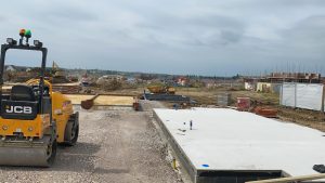 JCB ride-on compaction roller next to a freshly poured concrete foundation slab on a housing development site in Earls Barton Northamptonshire