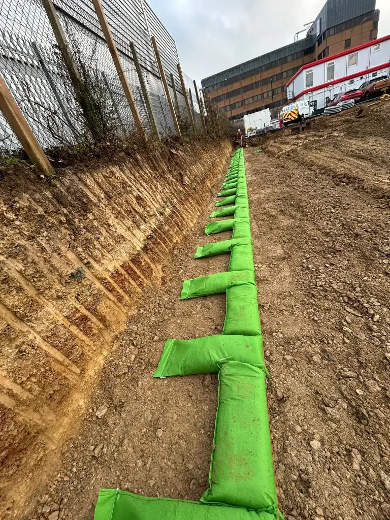 Green geotextile soil bags installed in an excavated trench for retaining wall construction in Preston Deanery