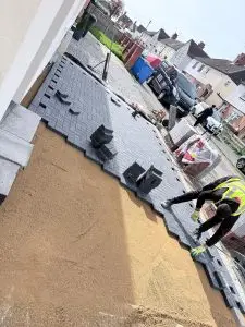 A worker laying heavy-duty block paving on a prepared sand base for a new driveway installation in Rothwell, Northamptonshire