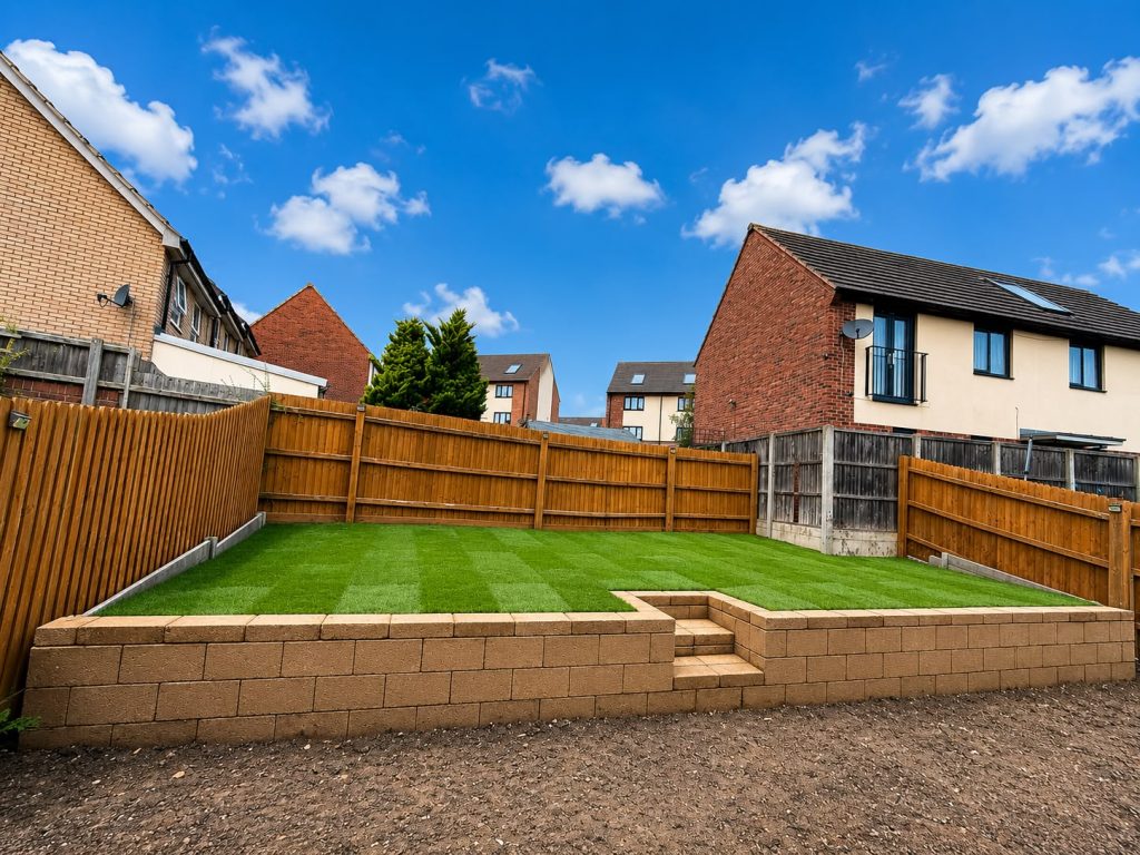 Completed tiered garden landscaping in Wellingborough featuring steps integrated into a concrete block retaining wall with a lush striped turf lawn