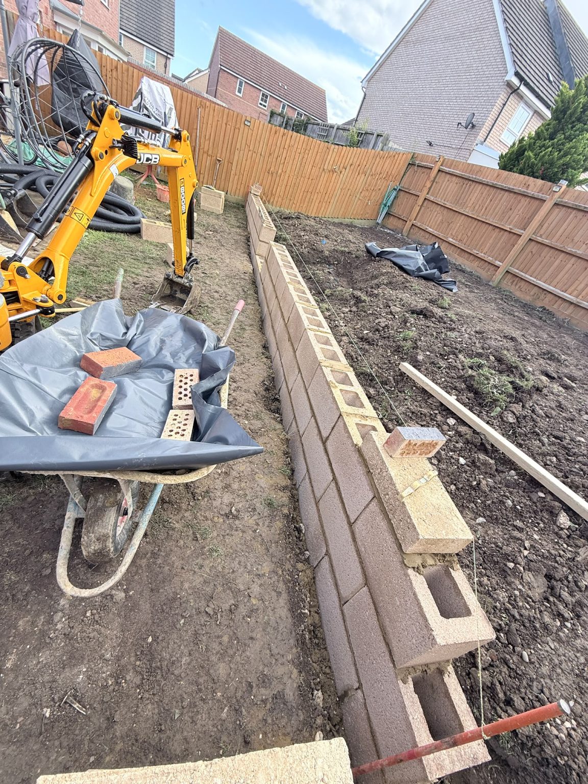 JCB mini excavator performing garden groundworks and block retaining wall construction in Wellingborough