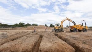 Construction workers and yellow excavator digging deep foundation trenches for groundworks in Northampton