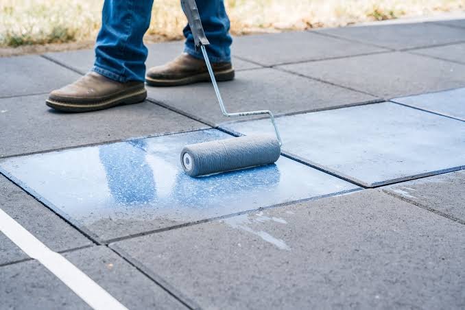 Applying protective sealant with a roller on stone patio paving slabs