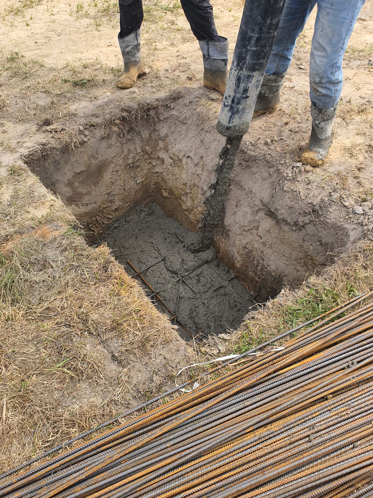 Builder directing concrete into an excavated foundation trench on a construction site